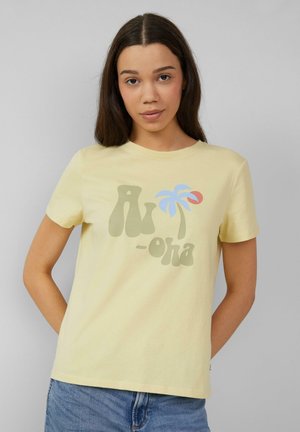 T-shirt en coton jaune avec un graphique amusant affichant "Aloha" en vert, un palmier bleu et un cercle rouge. Manches courtes, col rond.