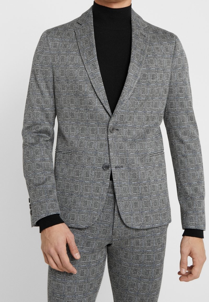Grijze gestreepte blazer met een subtiel ruitpatroon, notch-lapels, twee knopen en een slim-fit, gedragen over een zwarte coltrui.