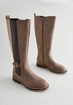 Braune kniehohe Stiefel mit einem glatten synthetischen Obermaterial, elastischen Seitenpaneelen, dekorativem Schnallenverschluss und strukturierten Gummisohlen für guten Halt.