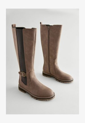 Brūni ceļgala zābaki ar gludu sintētisku augšdaļu, elastīgām sānu paneļiem, dekoratīvām sprādzēm un teksturētām gumijas zābaku apakšām, kas nodrošina saķeri.