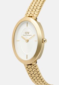 Reloj de oro con caja redonda, esfera blanca con patrón y correa de malla en tono dorado. Presenta marcadores de hora minimalistas y una corona en el lateral.