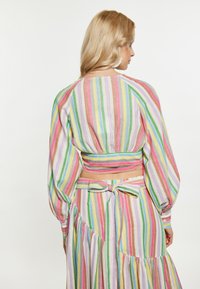 Tessuto a righe multicolori con colori pastello, caratterizzato da un design leggero e testurizzato. Maniche lunghe a sbuffo e dettaglio con laccio sul retro.