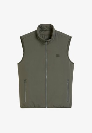 Bez rękawów kamizelka w oliwkowym kolorze, wykonana z miękkiego materiału. Posiada wysoki kołnierz oraz dwie boczne kieszenie na zamek. Gładka tekstura, minimalistyczny design.