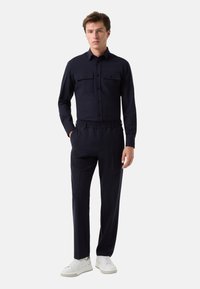 Chemise bleu marine à manches longues avec deux poches poitrine et des boutons, associée à un pantalon à taille élastique. Le mannequin porte des baskets blanches.