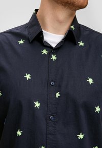Zwarte overhemdd met verspreide, groene bladborduursels over de stof, voorzien van een standaardkraag en een effen witte binnenlaag.