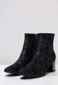 Botines negros de tela suave con un sutil estampado floral, puntera afilada, cremallera lateral y tacón cuadrado.