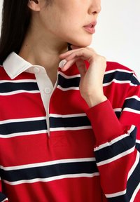 Rødstribet polo-shirt med hvide og navy blå striber, hvid krave og to knaplukninger, ribbede ærmer og tekstureret stof.