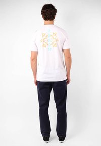 T-shirt blanc avec un motif floral coloré au dos, associé à un pantalon bleu marine. Le T-shirt a des manches courtes et une coupe régulière.