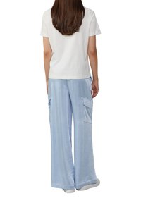 T-shirt en coton blanc et pantalon ample bleu clair avec poches cargo avant, texture lisse, taille élastique et léger brillant.