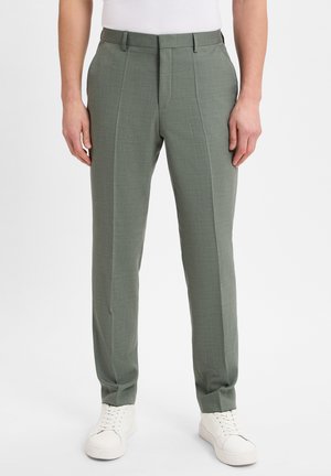 Hellgrüne maßgeschneiderte Hosen aus strukturiertem Stoff, mit flacher Vorderseite,Seitentaschen und schmaler Passform, kombiniert mit weißen Sneakern.