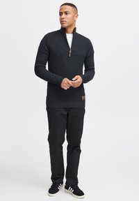 Zwart gebreid sweater met een halve rits kraag, geribbelde manchetten en een textuurpatroon. Gecombineerd met zwarte broek en donkere sneakers.