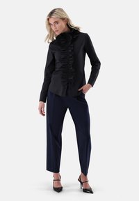 Black button-up shirt with a ruffled front, paired with navy pants and black stiletto heels. Smooth fabric, slim fit design.