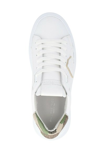 Witte sneaker met witte veters, beige merkteken aan de zijkant, en groen camouflagepatroon op de hielzoom, gezien van bovenaf.