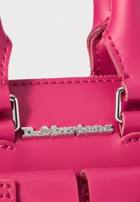 Pink polymer handbag featuring silver hardware, stitching accents, and a logo detail. Compact design with sturdy handles for easy carrying.