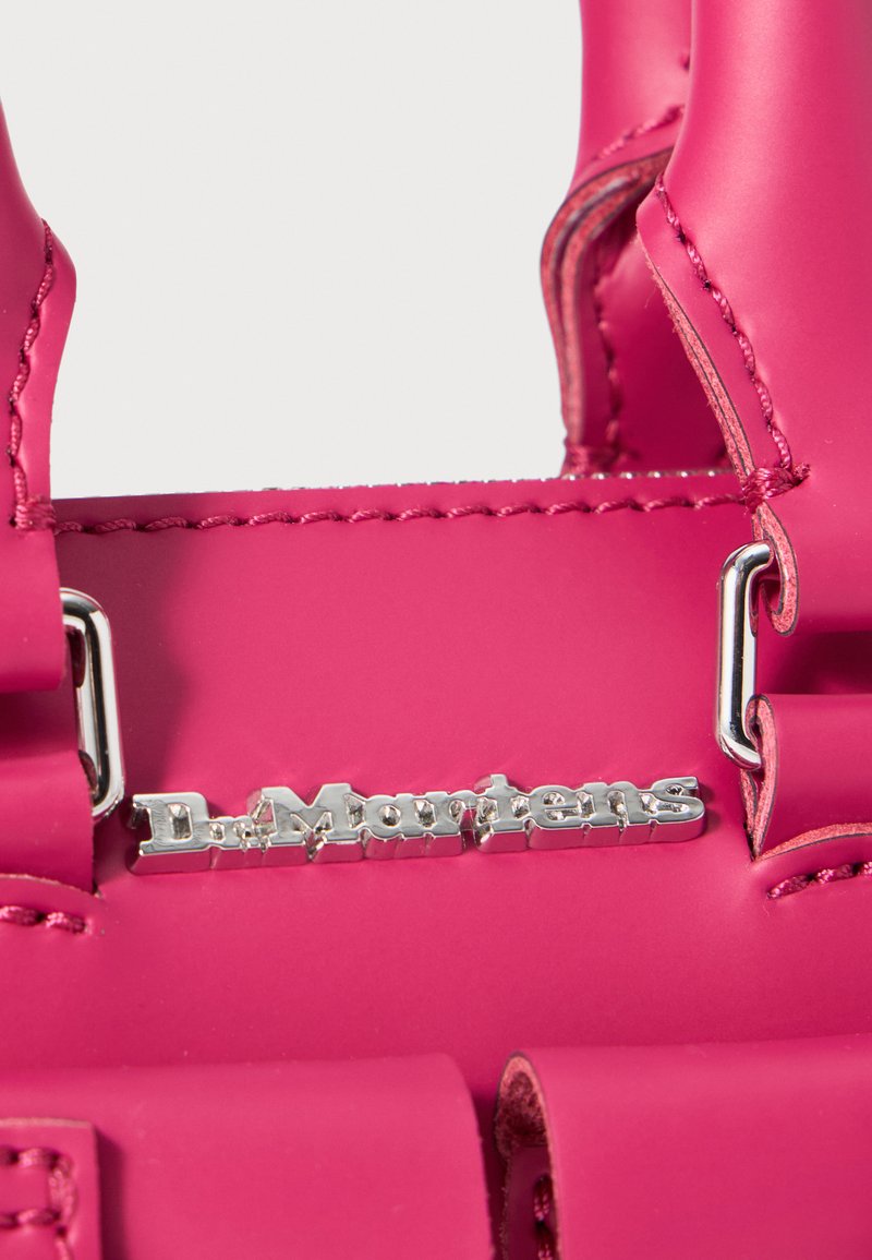 Sac à main en polymère rose avec quincaillerie argentée, accents de couture et détail de logo. Design compact avec des poignées robustes pour un transport facile.