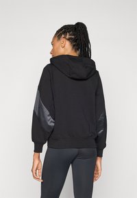 Felpa nera con cappuccio realizzata in tessuto texturizzato e dettagli in satin sulle maniche. Presenta una vestibilità rilassata e polsini a coste per il massimo comfort.