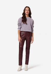 Lila Sweatshirt mit lockerer Passform, kombiniert mit bordeauxfarbenen Lederhosen mit gerippten Akzenten und weißen Knöchelschuhen.
