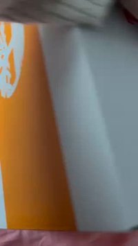 Embalagem retangular laranja e branca com um design gráfico na lateral, apresentando uma superfície lisa e sem hardware ou detalhes de textura visíveis.