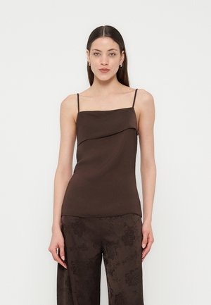 Kvinde med glat mørkt hår iført en ærmeløs mørkebrun top med tynde stropper og matchende bukser med blomstermønster.