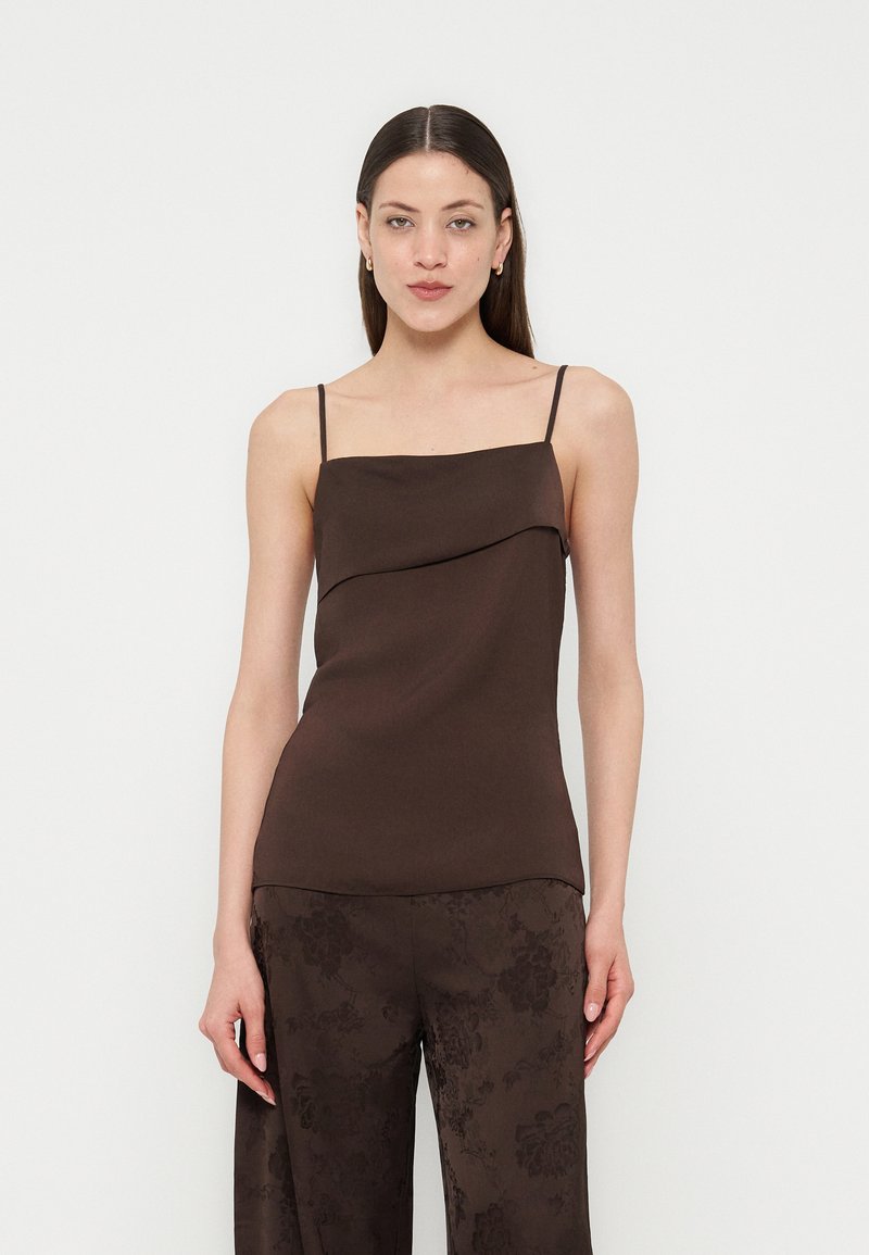 Γυναίκα με ίσια σκούρα μαλλιά που φοράει αμάνικο σκούρο καφέ τοπ με λεπτές τιράντες και ταιριαστό παντελόνι με φλοράλ σχέδιο.