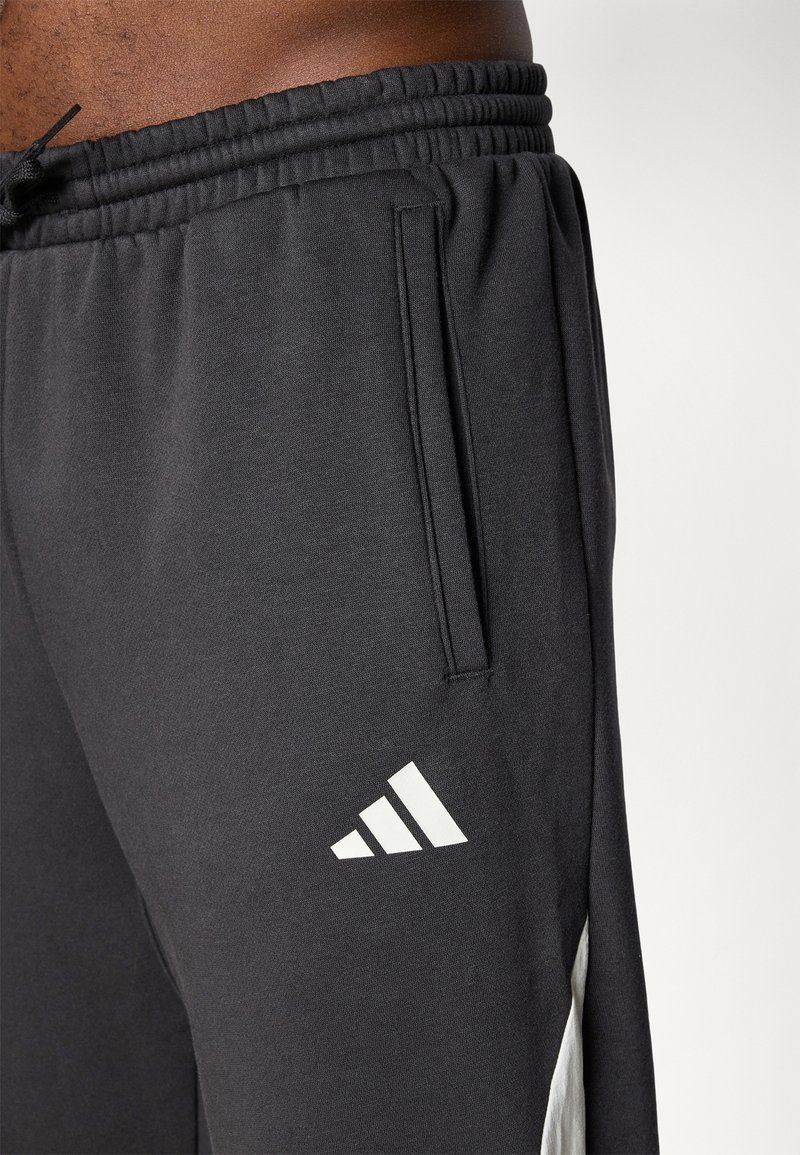 Czarne spodnie sportowe z elastycznym paskiem, bocznymi kieszeniami i białymi akcentami z logo. Wykonane z miękkiego, gładkiego materiału o luźnym kroju.