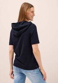 Sudadera corta de manga corta en azul marino con capucha con cordón, corte relajado y aberturas laterales en el dobladillo, combinada con jeans de mezclilla de lavado claro.