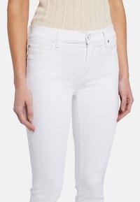 Jeans en denim blanc au design ajusté, avec une fermeture éclair et un bouton, une conception à cinq poches et des détails de broderie subtils.