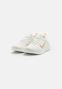 Hvide sportsko med en struktureret overdel, prydet med et guld Nike swoosh og gule accenter. Letvægtsdesign med en fleksibel sål.