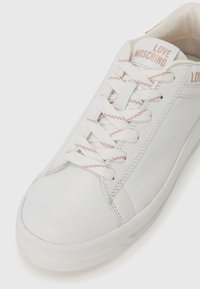 Valge nahast tennisetoss, ümarate varvastega, roosa aktsendiga nööridega ja "LOVE MOSCHINO" brändimisega keelel. Sile tekstuur ja minimaalne disain.