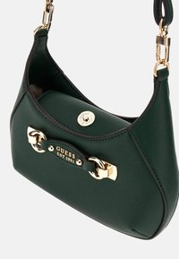 Sac à main en simili cuir texturé vert avec quincaillerie dorée, présentant un logo, une bandoulière en boucle et des bords arrondis. La fermeture est un bouton-pression.