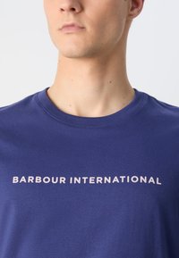 Navy blue short-sleeve t-shirt made of cotton, featuring a crew neckline and the text "BARBOUR INTERNATIONAL" in light pink across the chest.