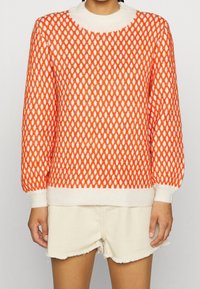 Pull en maille orange et blanc avec un motif en losanges texturé, un col rond, des poignets et un ourlet côtelés.