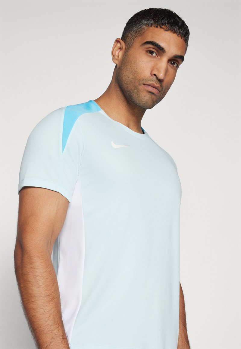 Helles blaues Sport-T-Shirt mit kurzen Ärmeln, das weiße und türkisfarbene Seitenteile sowie ein kleines weißes Logo auf der Brust zeigt.