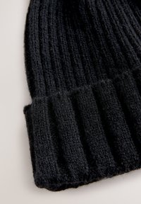 Bonnet noir en maille avec une texture côtelée et un revers plié. Le tissu semble doux et est principalement d'une couleur unie sans motifs visibles.
