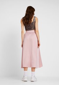 Avklippt leopardmönstrad topp med mjuk rosa, midikjol med sidostripes. Modellen bär vita sneakers och ankelsockar.