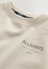 Sweatshirt beige avec col ras du cou côtelé. Présente le logo "ALLSAINTS" et un texte supplémentaire en japonais. Confectionné en tissu doux avec une texture lisse.