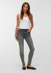 Jeans ajustados grises de cintura alta, con un leve desvanecimiento y bolsillos frontales, combinados con una camiseta sin mangas blanca y bailarina negra.