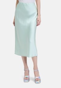 Jupe midi en satin vert menthe avec une texture lisse, présentant une silhouette droite et un éclat subtil. Assortie à des sandales à plateforme iridescentes.