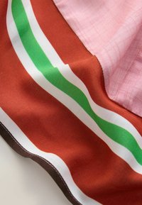 Kangas dengan garis miring berwarna merah muda, merah, dan hijau; memiliki tekstur yang halus; dikelilingi oleh border cokelat tua.
