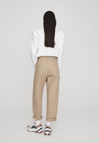 Pantalones beige de cintura alta con puños enrollados, combinados con zapatillas chunky blancas y multicolores. Detalle de mangas elásticas en una blusa blanca.