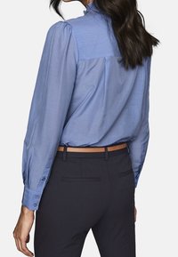 Light blue long-sleeve shirt with gathered shoulder seams, button cuffs, and a smooth texture, paired with dark trousers and a brown belt.
