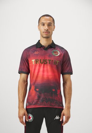 Polo-shirt à manches courtes rouge et noir avec un design dégradé, arborant "TRUST IT" en or, le logo Kappa et des graphiques détaillés sur le tissu.