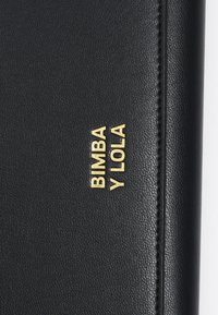 Cartera de cuero negro texturizado con el logotipo dorado en relieve "BIMBA Y LOLA". Presenta un diseño elegante y bordes cosidos. Estilo minimalista.