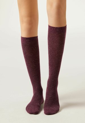 Knähöga strumpor i djup burgund med en subtil spräcklig textur. Tillverkade av mjukt tyg med en åtsittande design som når precis under knäet.