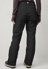 Black ski pants with a straight cut, made from a durable material. Features a back logo, zippered leg openings, and reinforced hems.