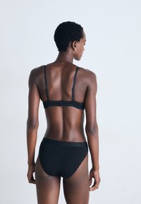 Black bra and panty set with adjustable straps, smooth fabric, minimalist design, and seamless edges, displayed from the back.