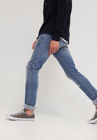 Jeans de denim desgastado en azul claro con un ajusteSlim, puños enrollados y una textura desvanecida, combinados con zapatillas de lona grises.