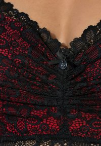 Zwart en rood kanten topje met bloemmotieven, geplooide stof bij de buste, geschulpte randen en een klein zwart lint met een labeldetail.