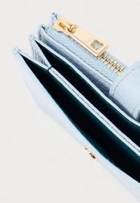 Ανοιχτό μπλε δερμάτινο πορτοφόλι με χρυσλό φερμουάρ και πολλαπλές ανοικτές θήκες σε λευκό φόντο.