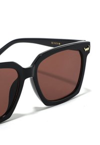 Černé sluneční brýle s oversized čtvercovými rámy, hnědými tónovanými skly a zlatým detailem ve tvaru vlny na stranici.